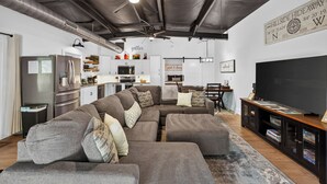 Una sala de estar moderna con un sofá modular, un televisor de pantalla plana y una cocina con electrodomésticos de acero inoxidable.