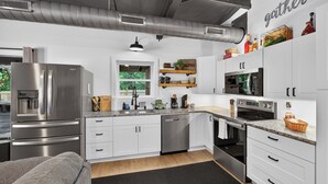 Una cocina moderna con muebles blancos, electrodomésticos de acero inoxidable y una alfombra negra.