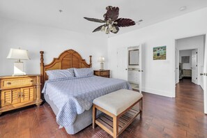 A bedroom with a wooden bed, a bench, a ceiling fan, a dresser, and a door leading to another room. - Gulf Front- Directly On The Beach- Sunchase 2A (Miramar Beach)