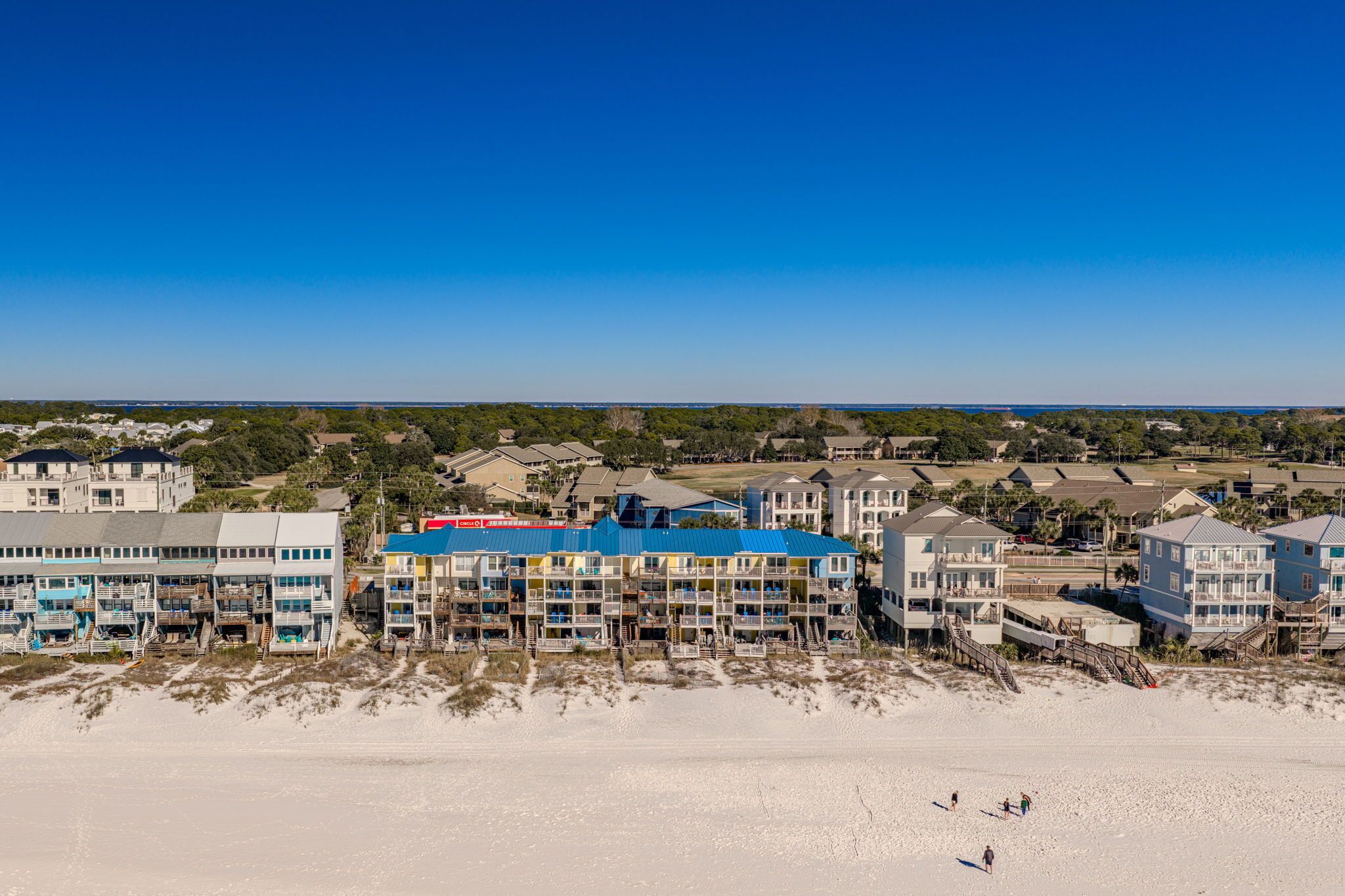 Et strandhotel med flere bygninger, heriblandt en markant bygning med blå tag, og en sandstrand i forgrunden.