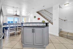 A spacious kitchen with a central island, a dining area with a table and chairs, and a staircase leading to an upper level. - Right On The Sand! Amazing Views! Sunchase 3A (Miramar Beach)