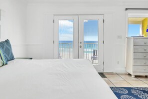 A bedroom with a large bed, a dresser, and a view of the ocean through a door. - Right On The Sand! Amazing Views! Sunchase 3A (Miramar Beach)
