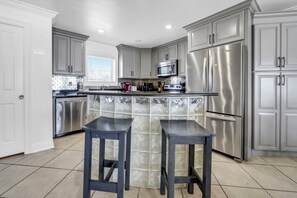 A modern kitchen with grey cabinets, stainless steel appliances, and a central island with stools. - Right On The Sand! Amazing Views! Sunchase 3A (Miramar Beach)