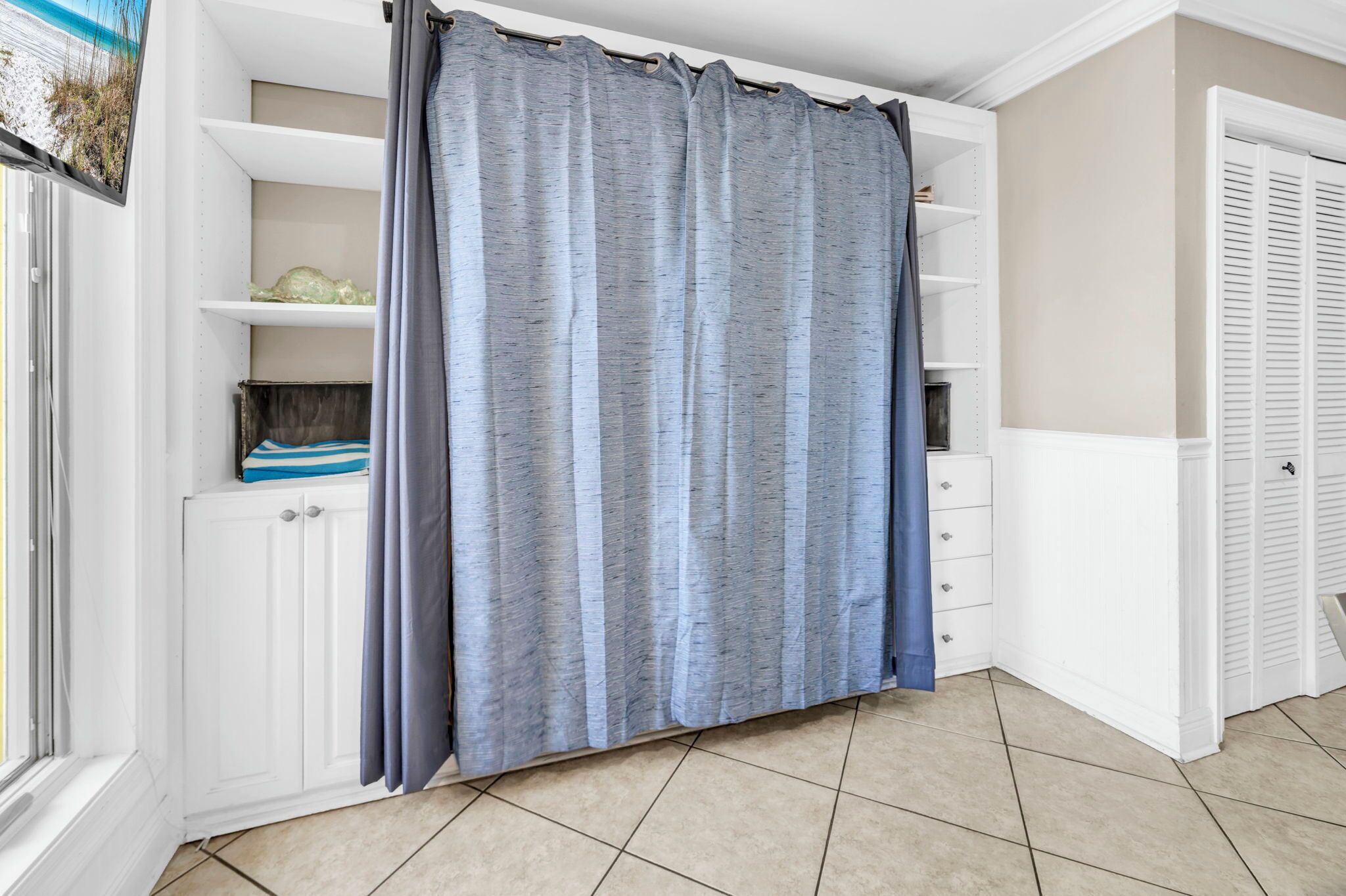 Ein Zimmer mit Fenster, Vorhang, einem weißen Schrank und einem Fliesenboden.