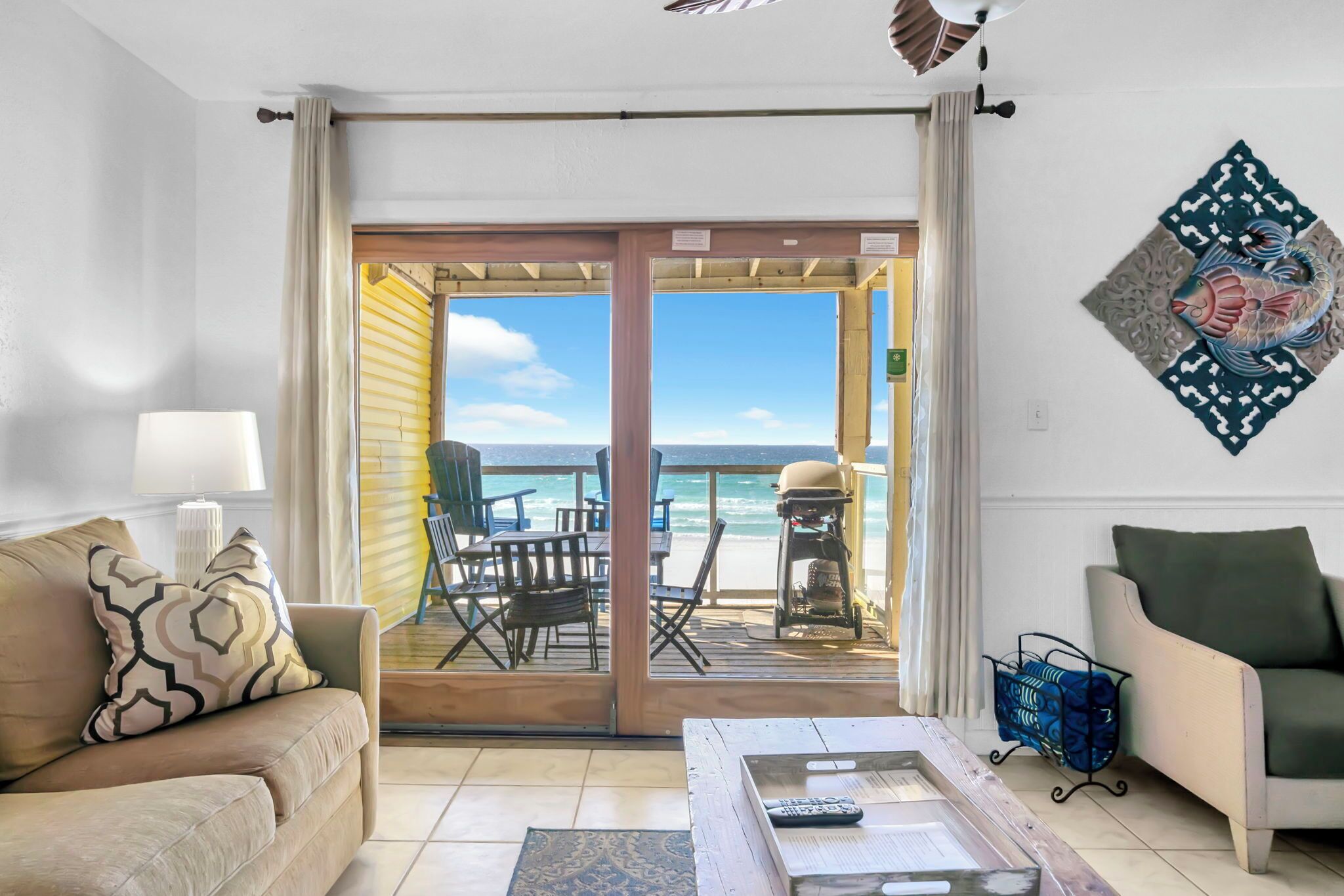 Habitación con sofá, una mesa de centro, una silla y vista a la playa a través de una puerta corrediza.