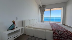 Ein Schlafzimmer mit einem großen Bett, einem Nachttisch, einem dekorativen Gegenstand, einer gemusterten Tagesdecke und Meerblick durch eine Schiebetür.