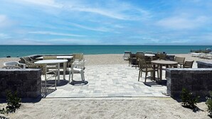 En uteplats vid stranden med utomhusmöbler och utsikt över havet.