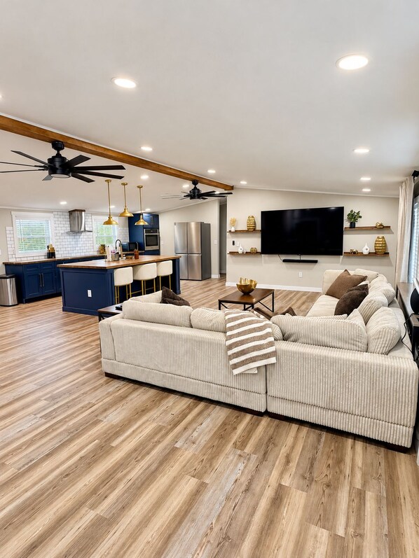 A modern living room with a sectional sofa, a flat-screen TV, and a ceiling fan.