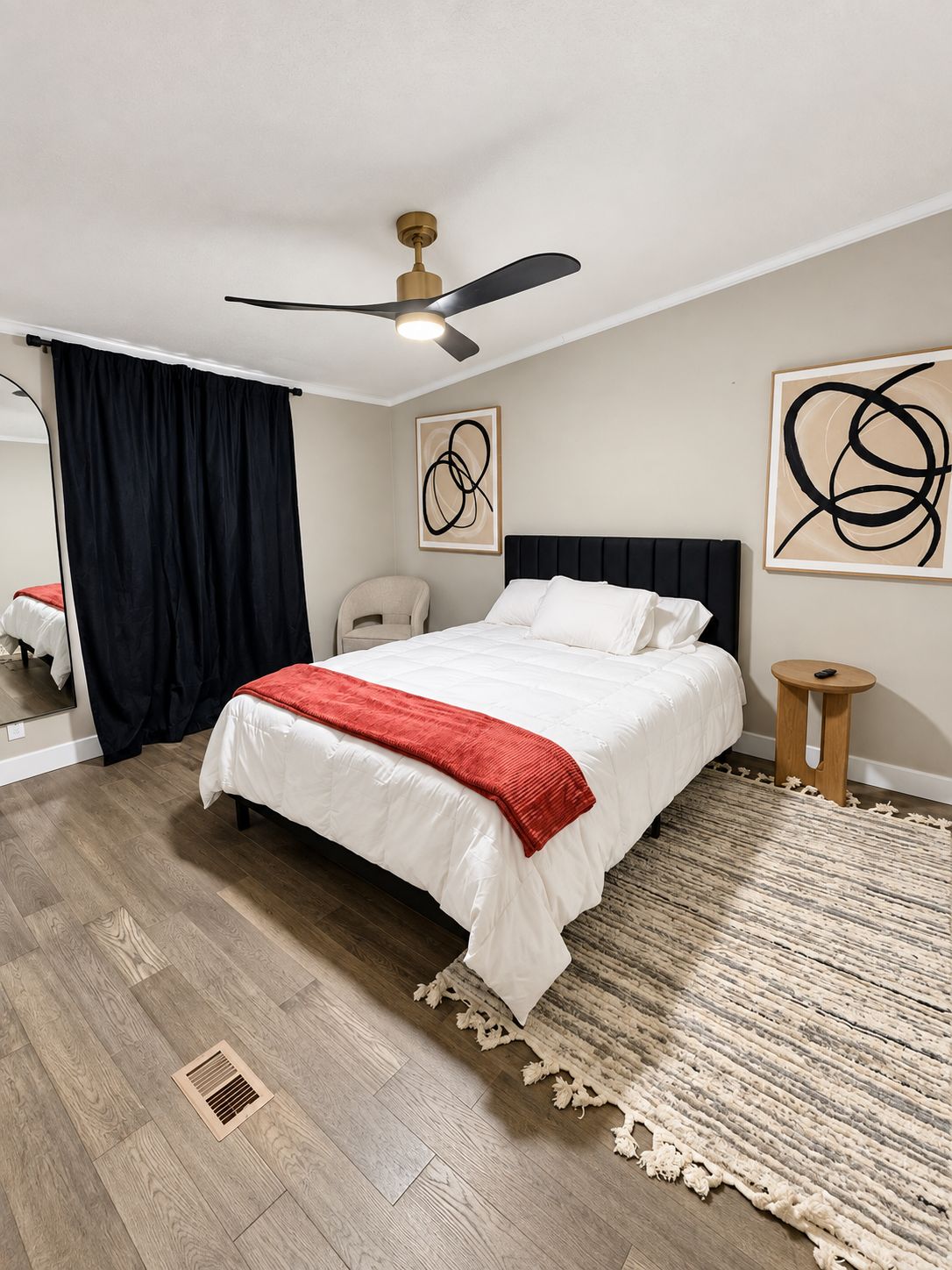 Un dormitorio con cama, ventilador de techo, silla, alfombra y obras de arte en las paredes.