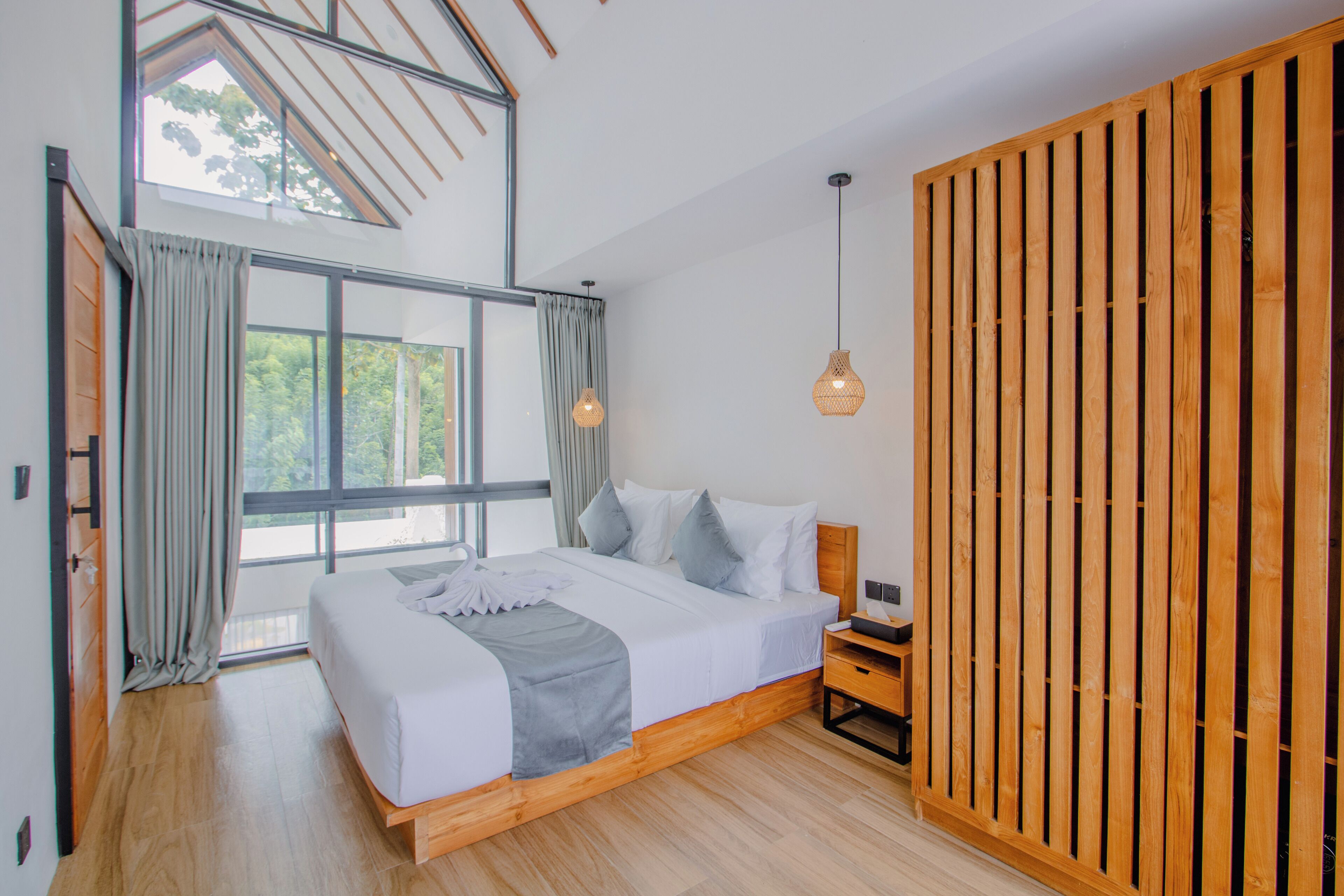 Camera da letto moderna con un letto grande, una testata in legno e vista sugli alberi dalla finestra.