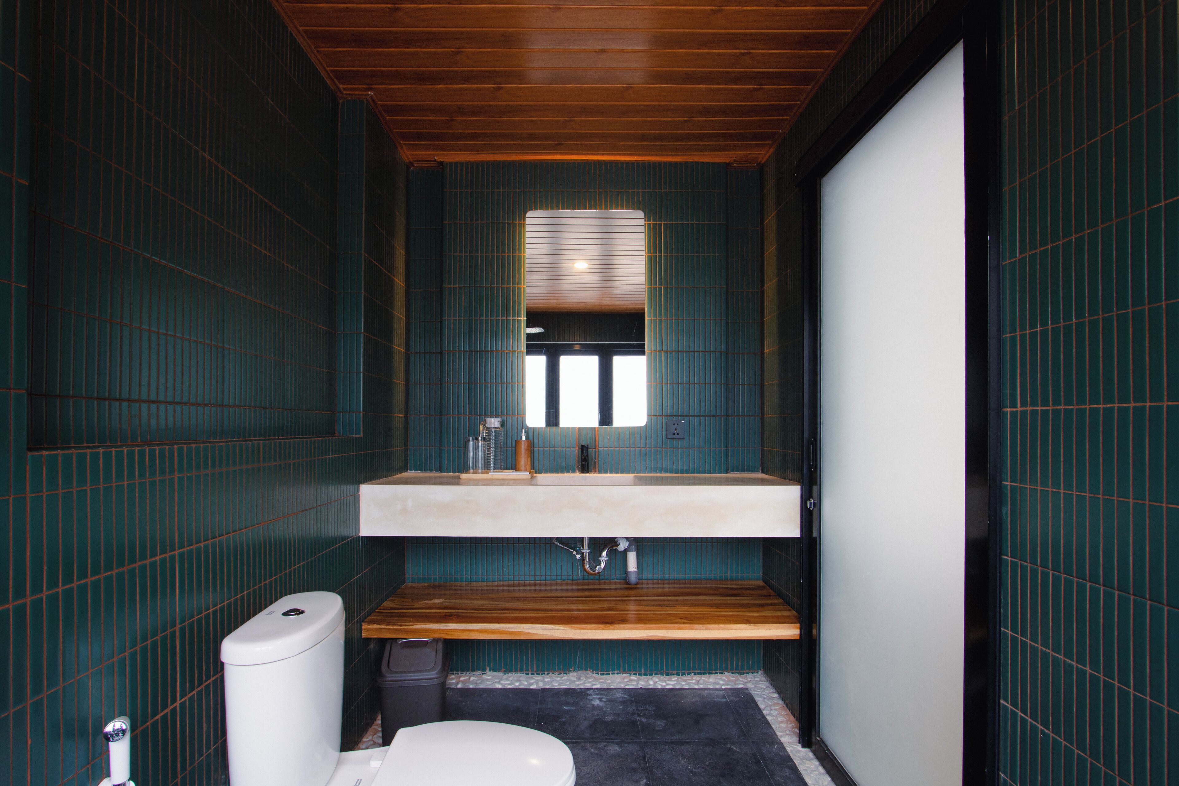 A compact bathroom with a wooden vanity, a white toilet, and a tiled backsplash.