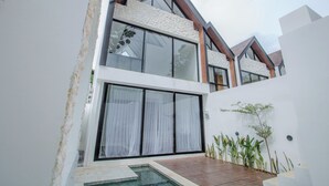 Une maison moderne à deux étages, dotée de grandes baies vitrées, d’une terrasse en bois et d’une petite piscine.