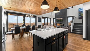 Une cuisine moderne dotée d’un grand îlot central, d’un plafond en bois et de grandes fenêtres offrant une vue sur le désert.