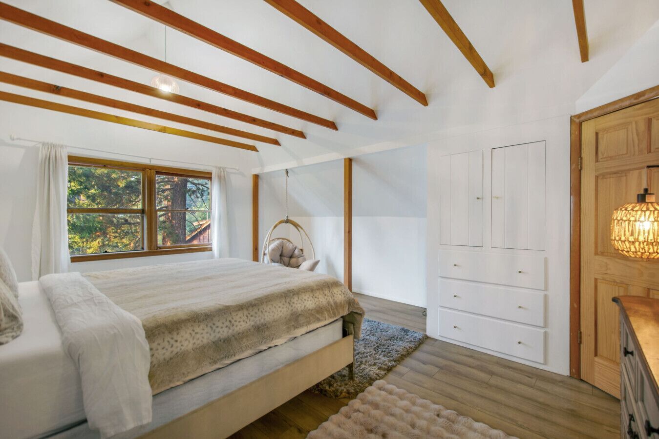 Een slaapkamer met een groot bed, houten balken, een raam met uitzicht, een hangstoel en een kledingkast.