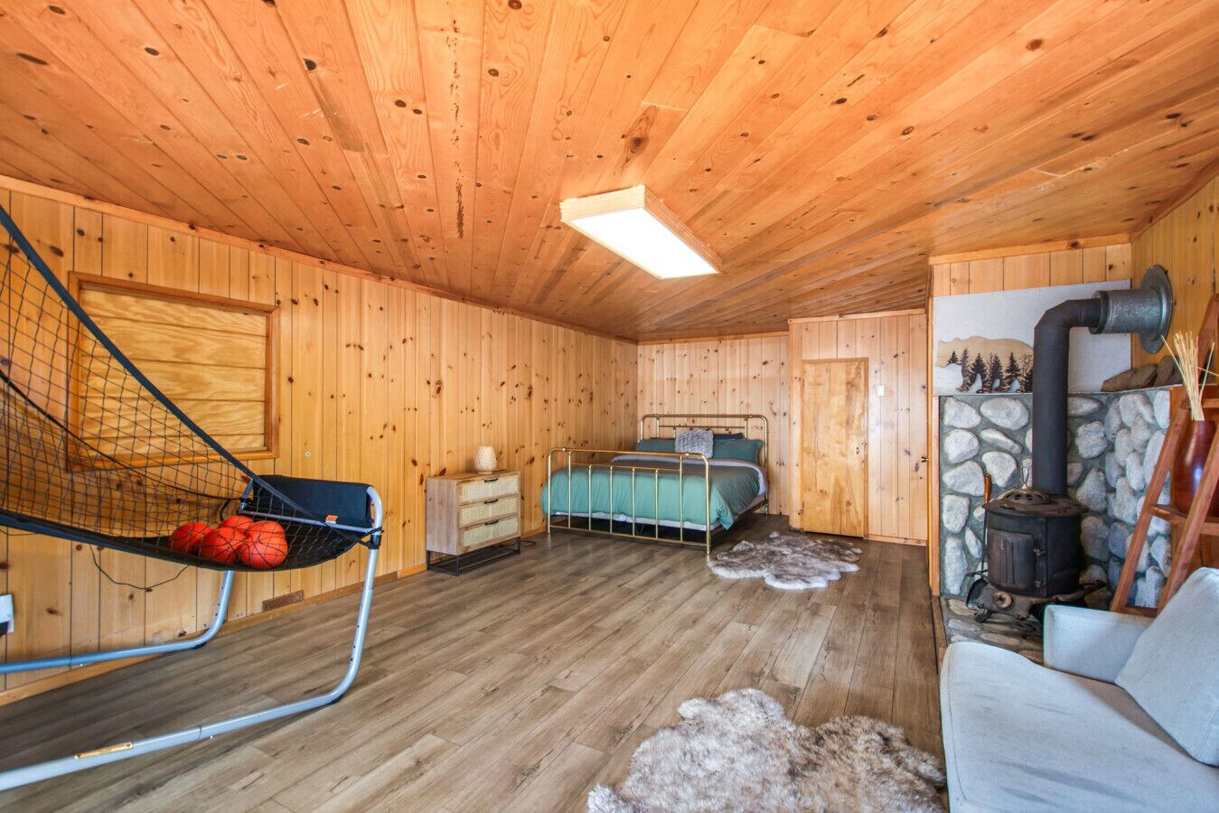 Ein gemütliches Blockhäuschenzimmer mit Etagenbett, einer Hängematte, einem Kamin aus Naturstein und rustikalem Holzinterieur.