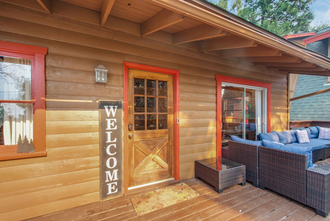 Une cabane en bois avec une pancarte « BIENVENUE », une porte en verre et un porche couvert agrémenté de meubles en osier.