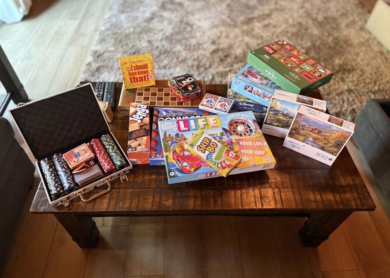 Une table en bois, sur laquelle on trouve divers jeux de société, et une valise.