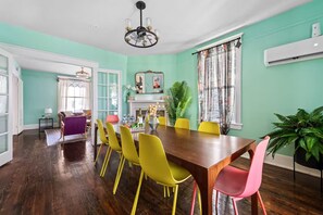 Un coin repas avec une table et des chaises en bois, un lustre et une grande fenêtre agrémentée de rideaux.