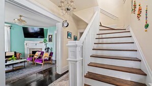 Eine Treppe mit weißen Geländern und Holzstufen, ein Wohnzimmer mit Kamin, Fernseher und einer Chandelier.