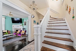 Un escalier avec des rampes blanches et des marches en bois, un salon avec une cheminée, un téléviseur et un lustre.