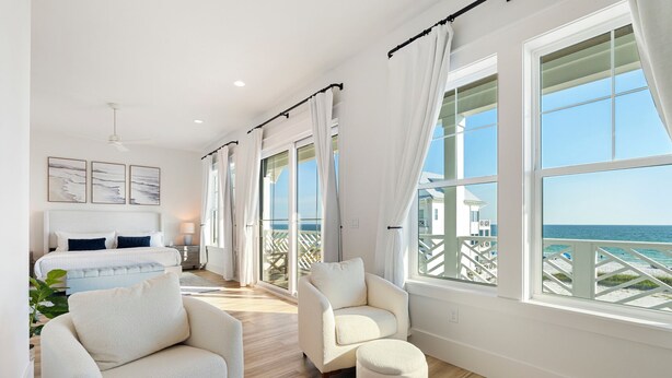 Un'ampia camera da letto con un letto grande, un angolo salotto con una poltrona e poggiapiedi, e un balcone con vista sull'oceano.