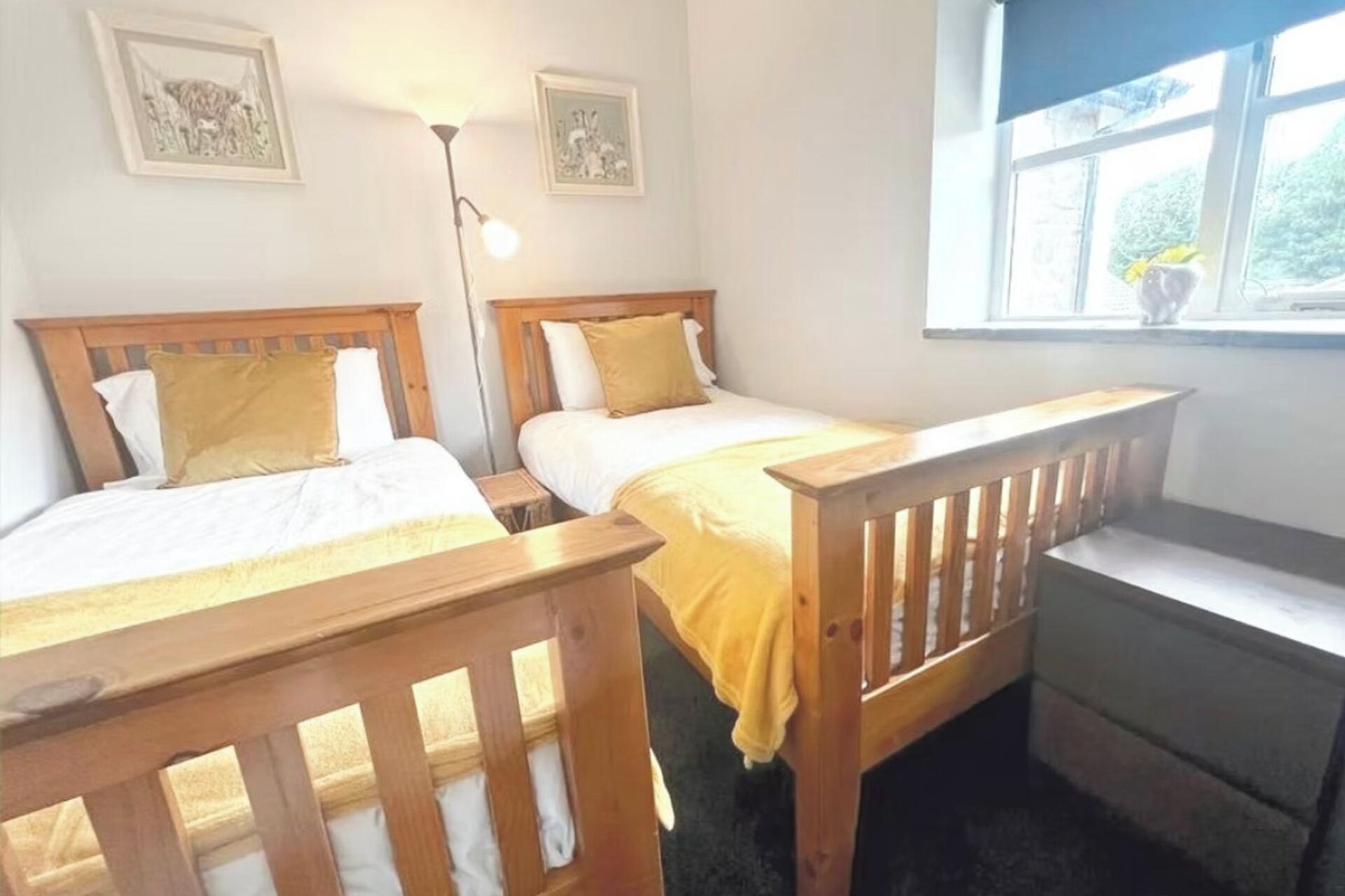 A room with two wooden beds, a nightstand, a lamp, and a window with a view of greenery.