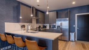 Uma cozinha moderna com ilha central, banquetas, eletrodomésticos de aço inoxidável e uma parede de destaque azul-escuro.