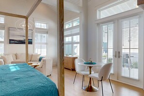 A modern bedroom with a large bed, a dining area with a table and chairs, and large windows with blinds. - Shared Pools, Boardwalk to the Beach (Port Aransas)