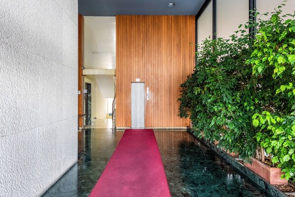 Un couloir recouvert d’une moquette rouge mène à une pièce dont un mur est recouvert de panneaux de bois et qui est dotée d’une porte en métal.