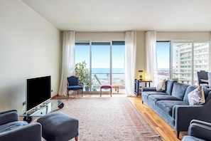 A living room with a sofa, armchairs, a TV on a glass table, a view of the ocean, and a balcony with a plant. - Piazza Rossetti 3A/8, Genova, Italy (Genova)
