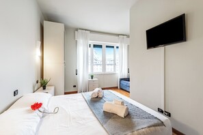 A hotel room with a bed, a TV, a window with curtains, a small table with a plant, and a blue chair. - Piazza Rossetti 3A/8, Genova, Italy (Genova)
