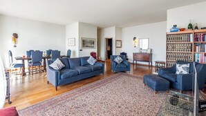 Ein geräumiges Wohnzimmer mit einem blauen Sofagarnitur, einem gemusterten Teppich und einem Bücherregal voller Bücher.