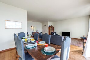 Un coin repas avec une table en bois dressée pour quatre personnes, entourée de chaises recouvertes d’un tissu bleu.