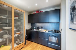 Une cuisine moderne dotée d’un plan de travail noir, d’appareils électroménagers en acier inoxydable et d’un meuble de rangement avec une façade en verre.