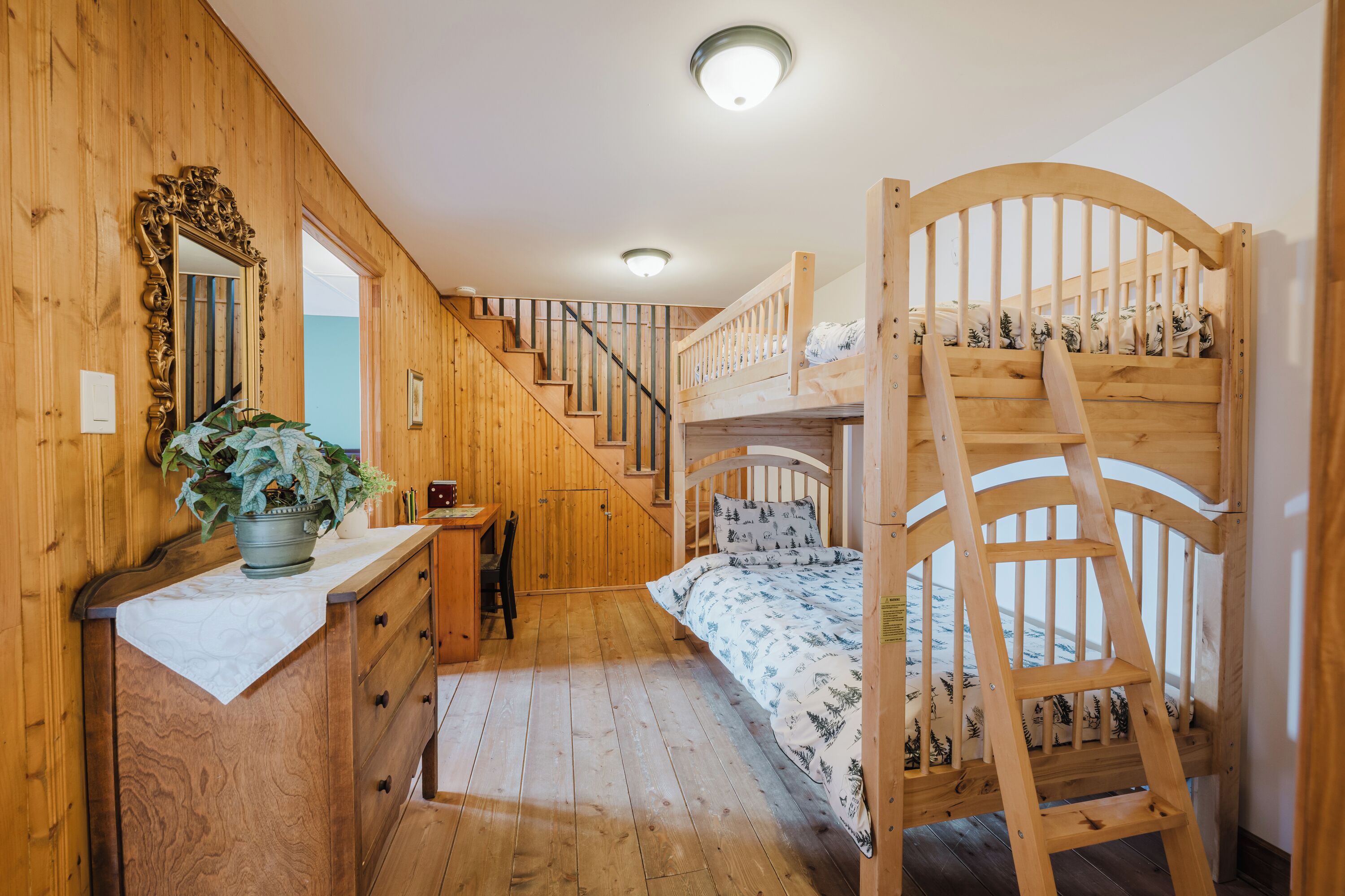 Un intérieur en bois comprenant un lit superposé, un bureau, une chaise, un miroir et un escalier.