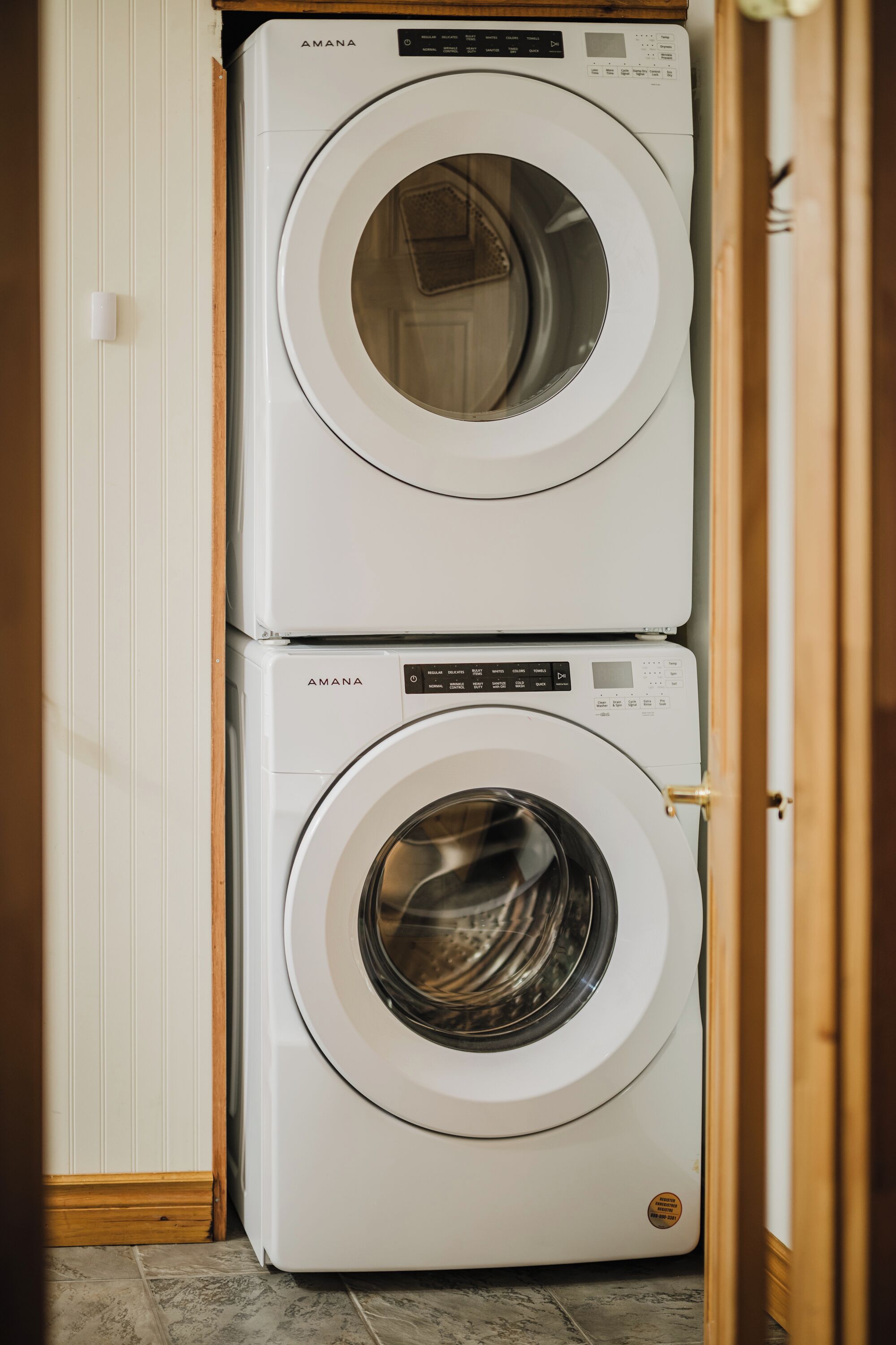 Dos lavadoras blancas apiladas en una habitación con suelo de madera y una puerta blanca.