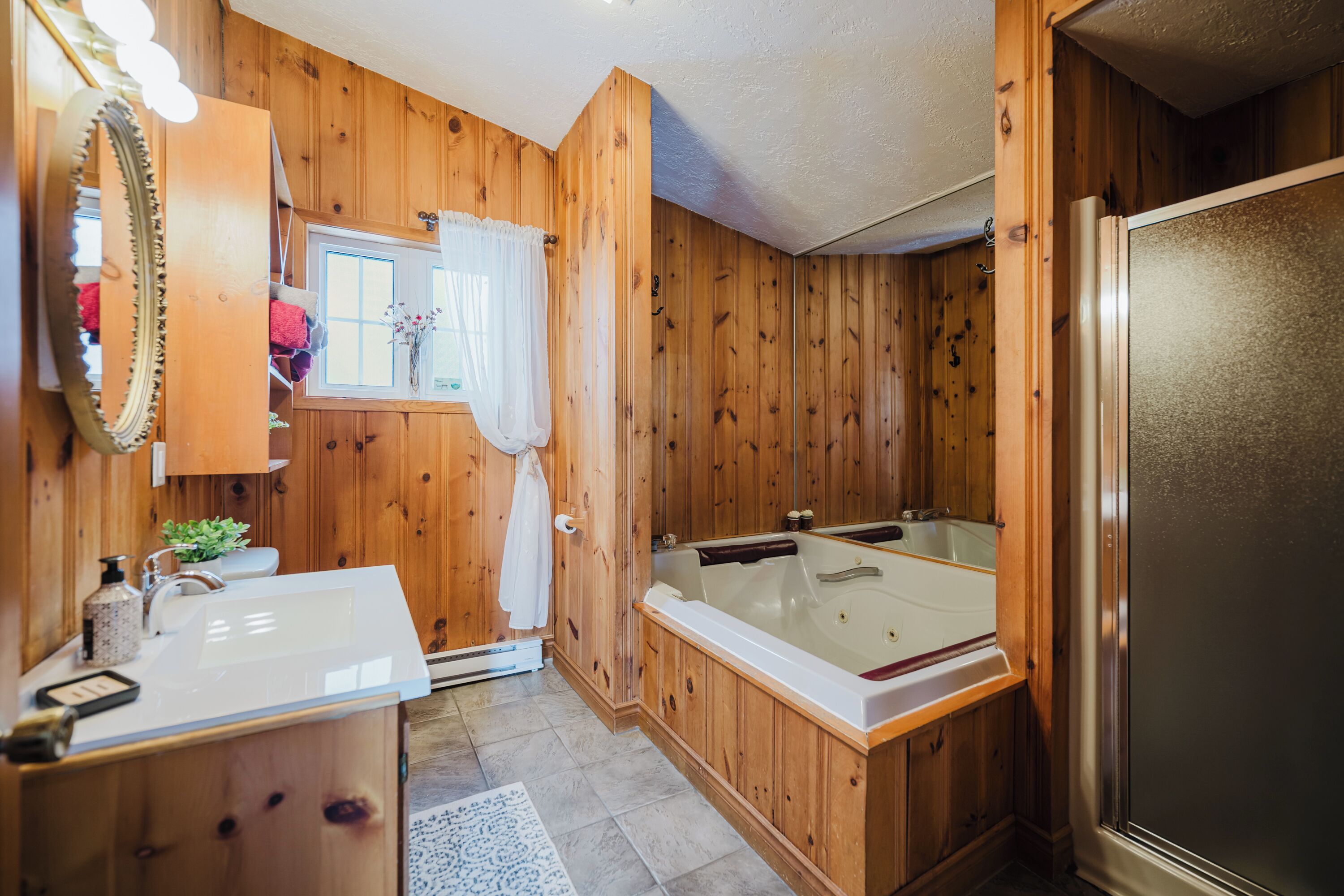 Een badkamer met houten lambrisering, een wastafel, spiegel en bad.
