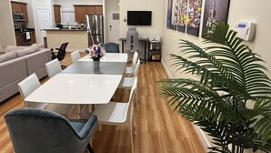 Uma sala de estar moderna com área de jantar, cozinha ao fundo e uma planta grande.