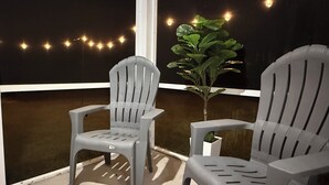 Duas cadeiras de plástico cinza numa varanda com um vaso de planta e luzes de cordão.