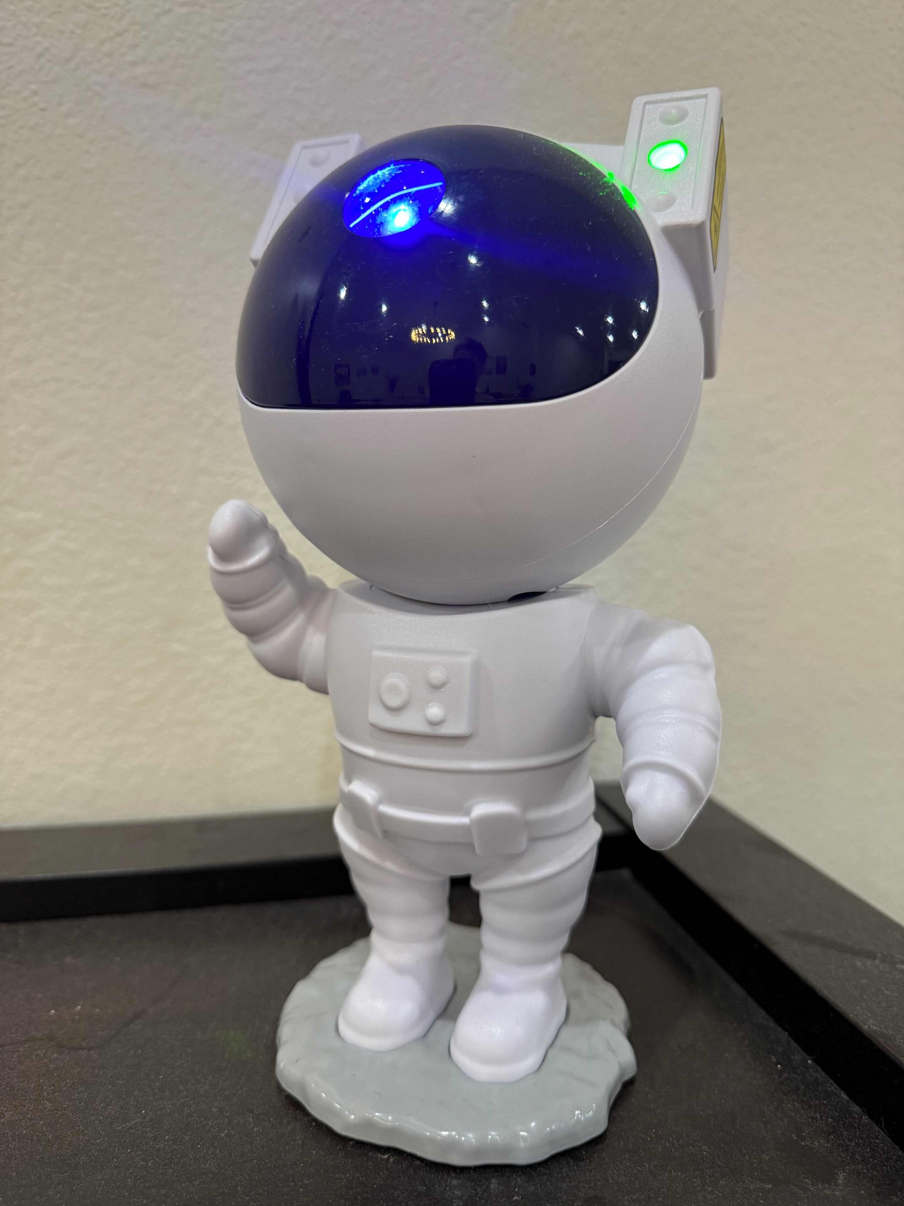 A white astronaut figurine with a reflective dome head and a green light on the side, standing on a base.