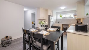 Una cocina moderna con una mesa de comedor para cuatro, armarios de color claro, un refrigerador y un microondas.