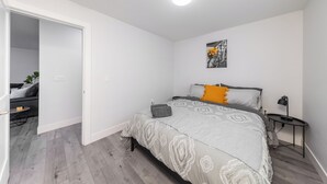 Un dormitorio con cama, mesita de noche, lámpara y un cuadro en la pared.