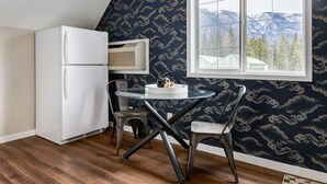 Une cuisine compacte avec un réfrigérateur blanc, une petite table avec deux chaises et une fenêtre donnant sur la montagne.