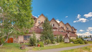 Un immeuble résidentiel à plusieurs étages, doté d’une façade en pierre, de nombreux balcons et d’un jardin bien entretenu avec des arbres et des arbustes.