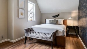 Une chambre à coucher avec un grand lit, un banc, une table de chevet, une lampe et une fenêtre décorée avec une lettre « C ».
