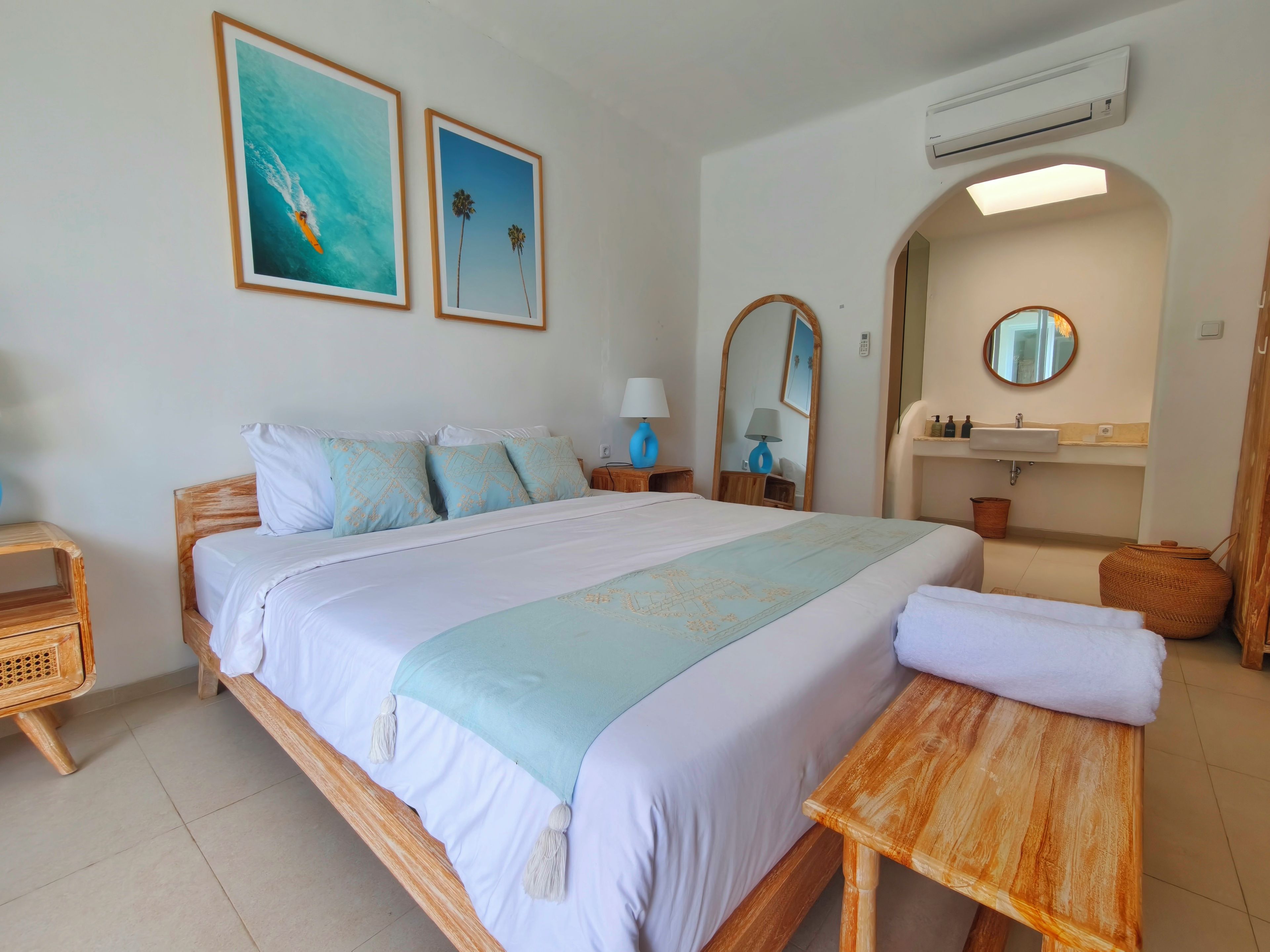 A hotel room with a bed, a bedside table, a mirror, a sink, and a wall-mounted air conditioner.