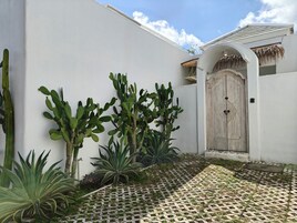 Um pátio com piso estampado, porta de madeira e diversas plantas, incluindo cactos e agave.