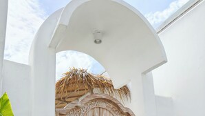 A white arched doorway with a wooden door featuring intricate carvings. - Villa Chioni Uluwatu (Ungasan)