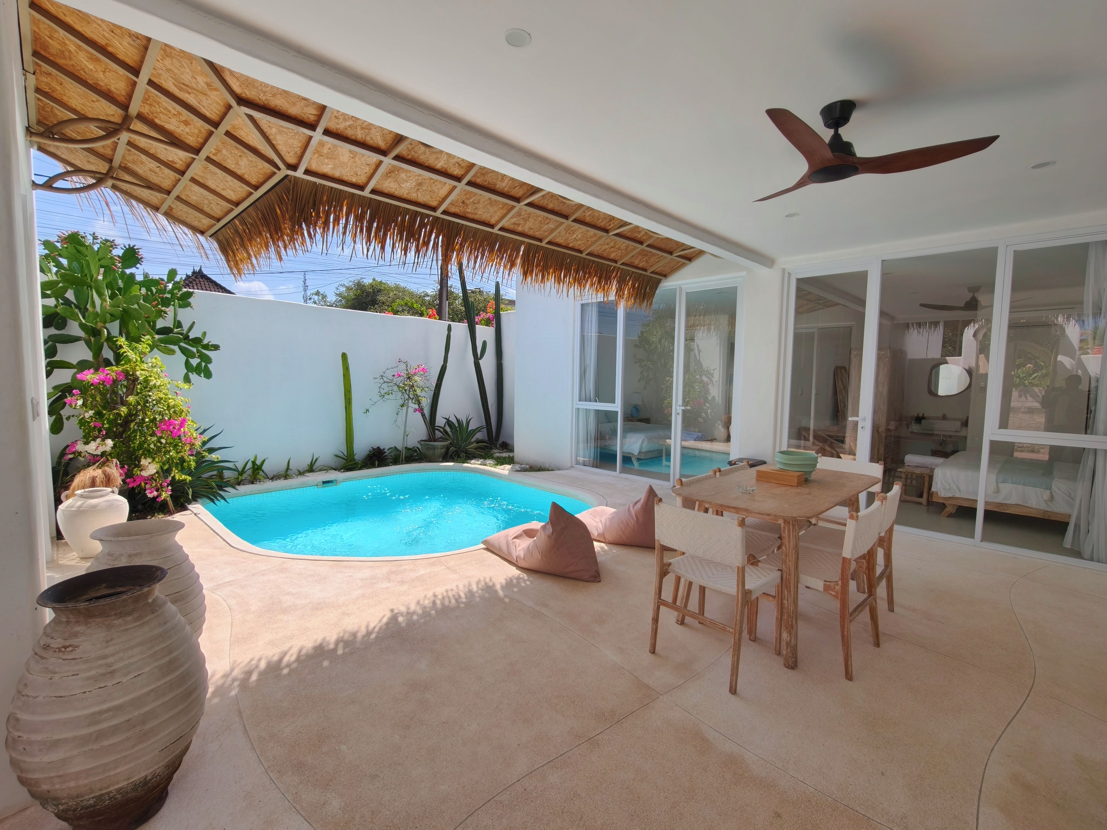A poolside area with a table and chairs, a ceiling fan, and a large window.