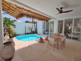 Un área junto a la piscina con mesa y sillas, un ventilador de techo y un ventanal grande.
